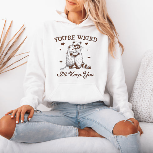 Celebrate the beauty of quirky connections with our comfy hoodie, featuring an adorable illustration of a raccoon and possum sharing a heartwarming hug.